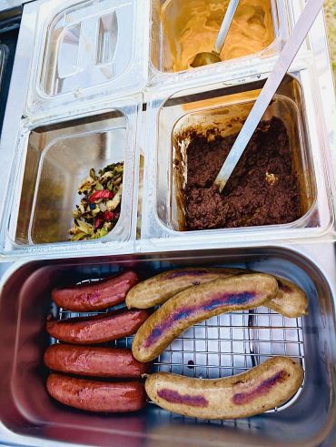 Grilled sausages with various condiments in containers.