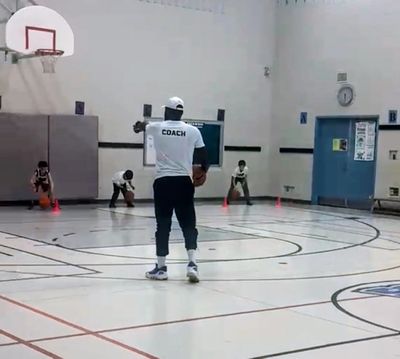 A coach trains young basketball players in an indoor gym.