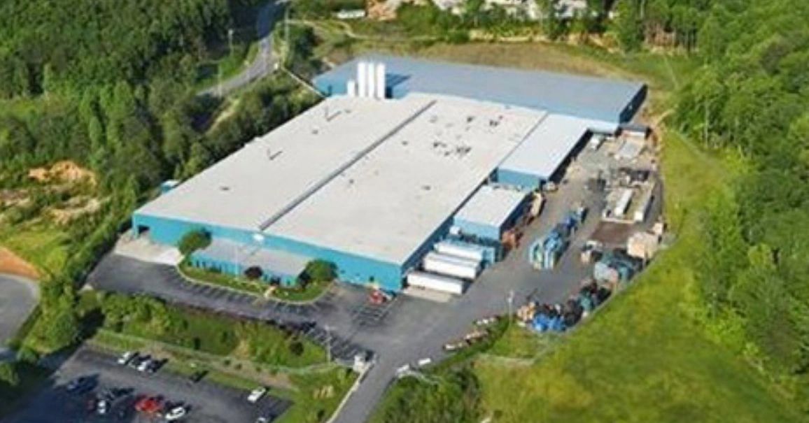 A large industrial warehouse surrounded by greenery and parking areas.