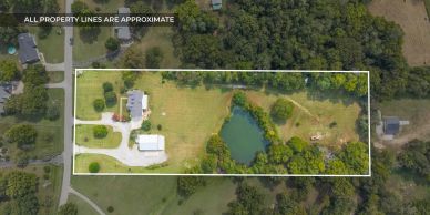 Aerial view of a rectangular property with a house, pond, and trees.