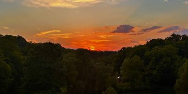 A vibrant sunset over a wooded landscape with a small pond below.