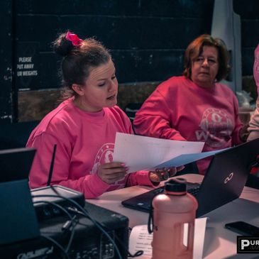 Two women in pink shirts reviewing papers at a table with laptops.