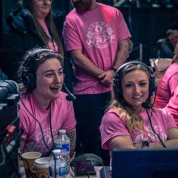 Two commentators wearing headsets and pink shirts at an event.