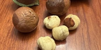 Whole and shelled macadamia nuts on a wooden surface.