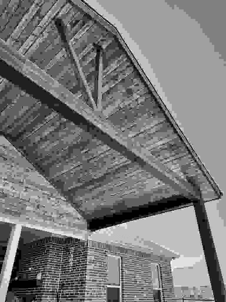 Wooden pergola roof attached to a brick house under clear blue sky.
