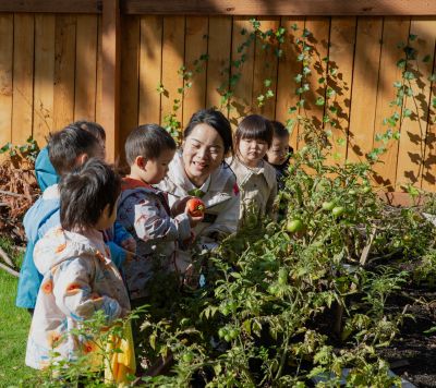 Teacher showing kids a ripe tomato in garden.