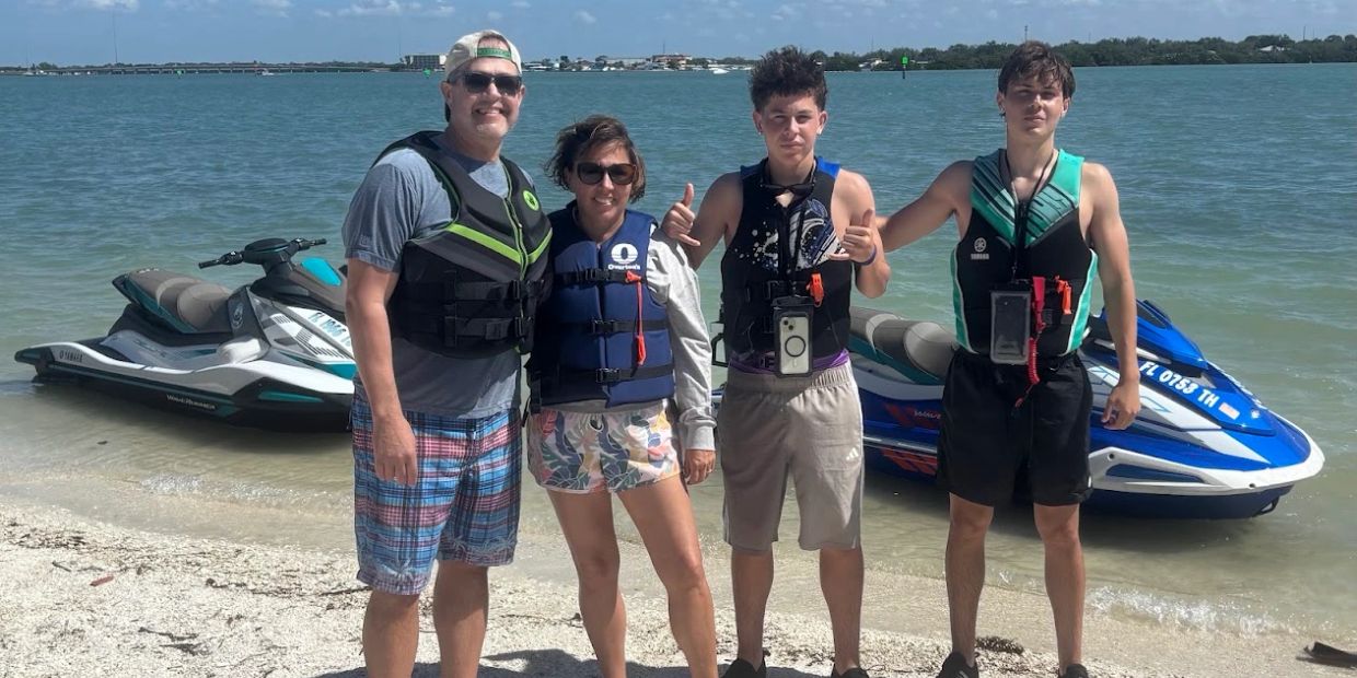 Family of four posing by the beach with jet skis.