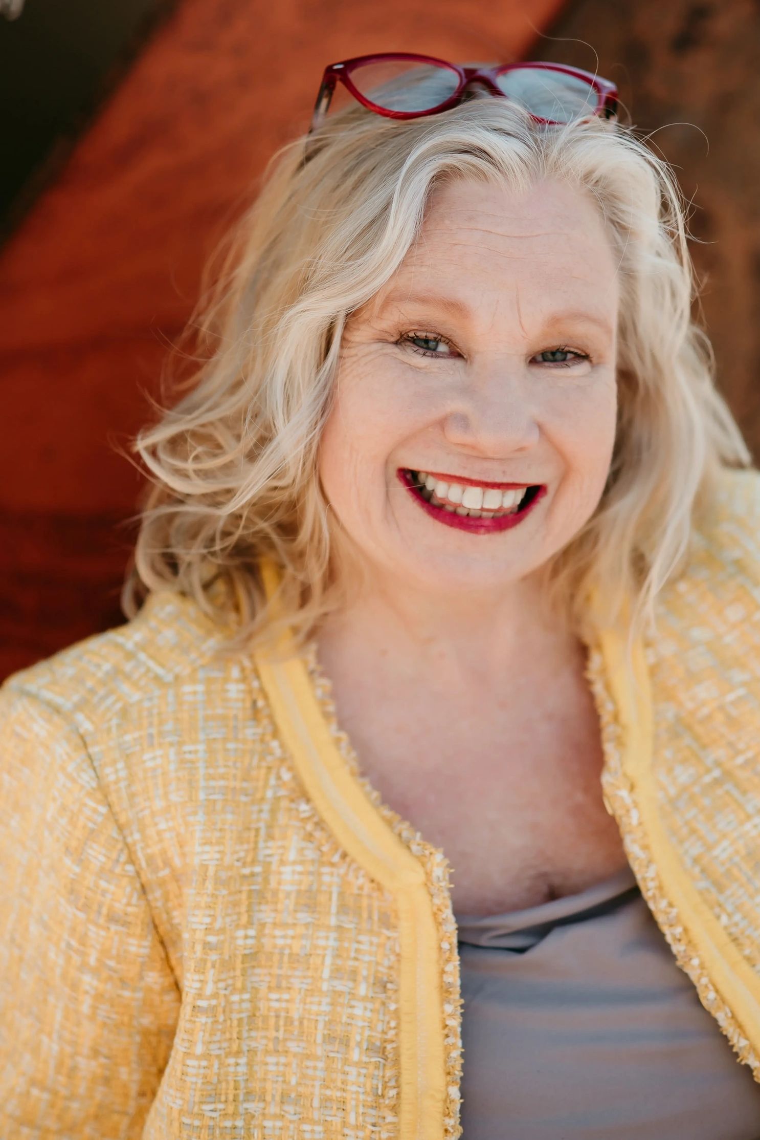 Smiling woman with blonde hair and red glasses on her head.