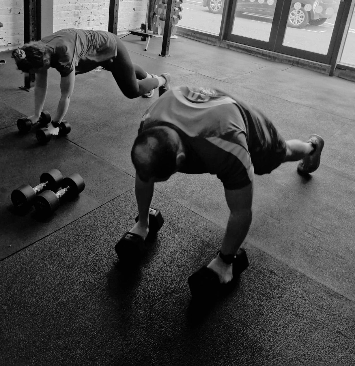 Two individuals performing mountain climbers using dumbbells in a gym.