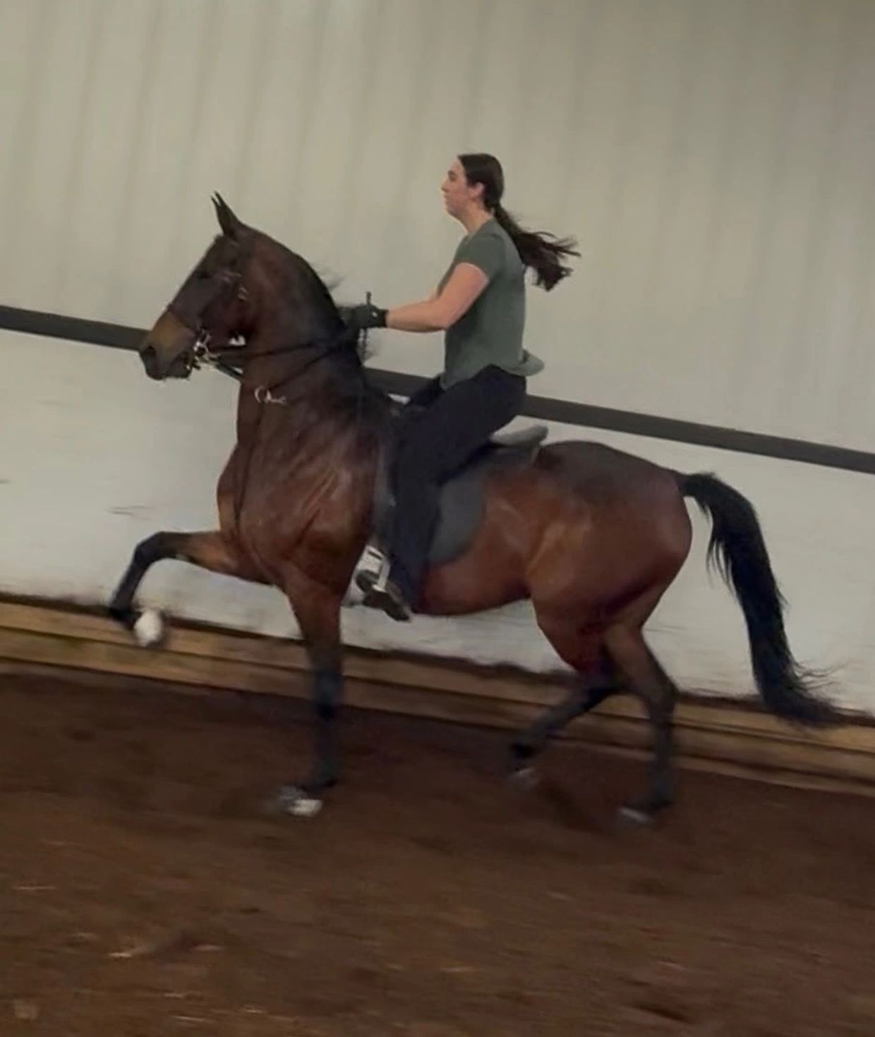 A woman riding a horse indoors with controlled posture.