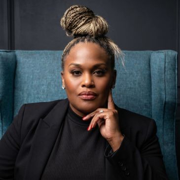 Confident woman with braided hair sitting in a teal chair.