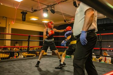 Two young boxers sparring in a ring under referee supervision.