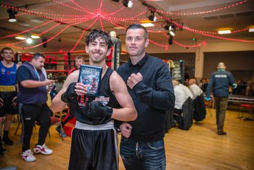 Young boxer proudly holding a trophy with his coach in a decorated gym.