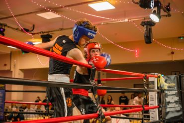 Two young boxers sparring in a well-lit boxing ring with spectators watching.