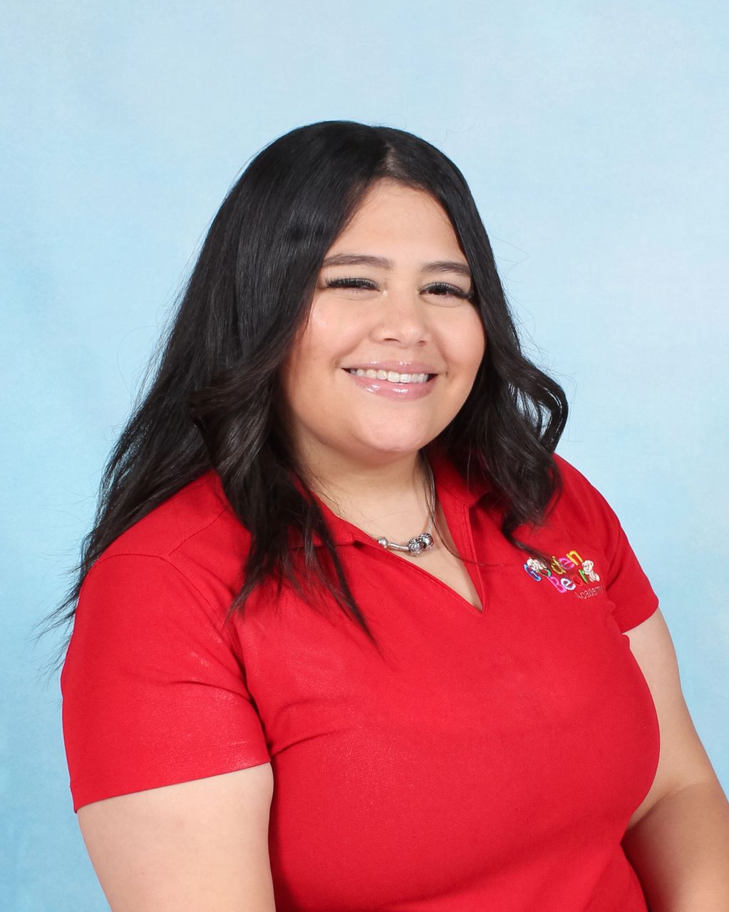 Smiling woman with long black hair wearing a red polo shirt against a blue background.