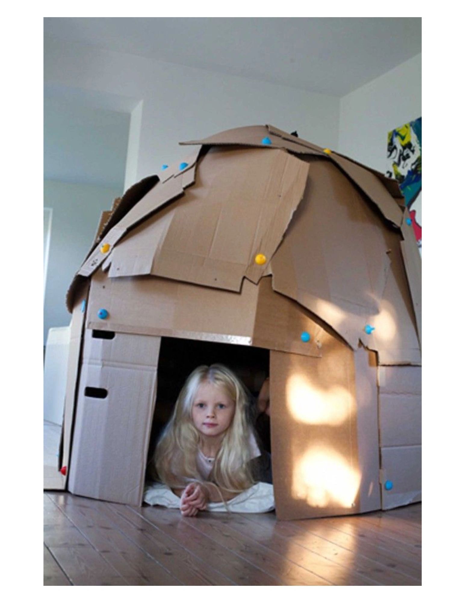 Child playing inside a homemade cardboard fort.