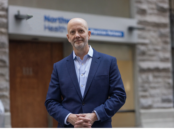 Brett Miles MD wearing a suit standing on a sidewalk in NYC with a clinical building behind him.