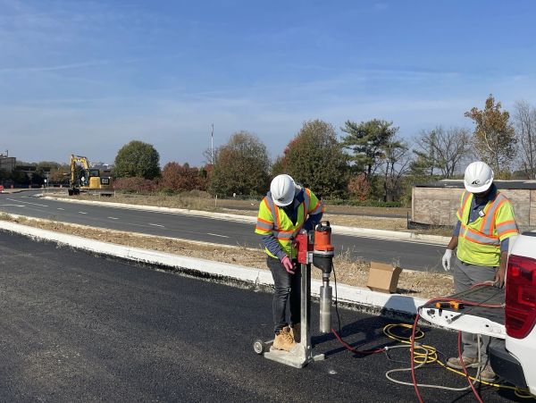 Two workers in high-visibility vests operating equipment on a road.