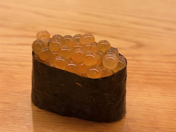 Close-up of salmon roe sushi wrapped in seaweed on a wooden surface.