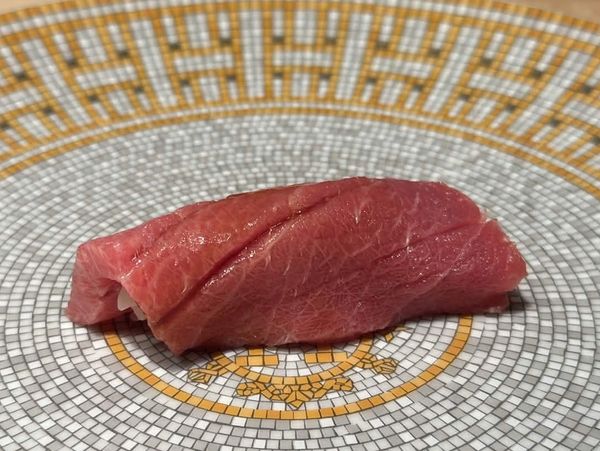 Piece of nigiri sushi with fresh tuna on decorative plate.