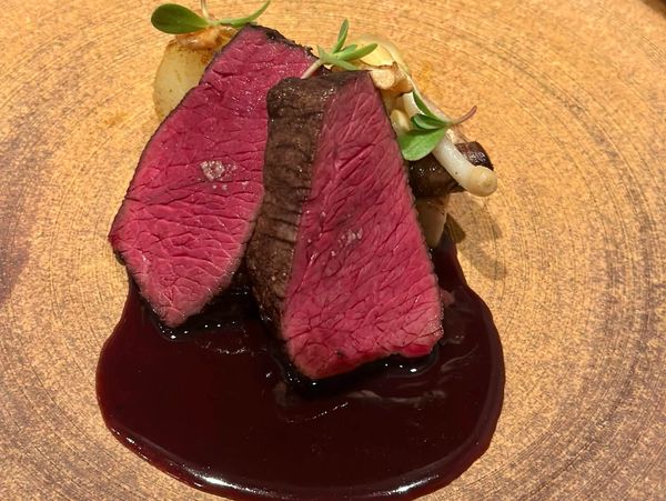 Two slices of rare steak served with dark sauce and garnished on a wooden plate.