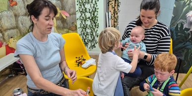 Two women and three children engaged in painting and playing in a colorful room.