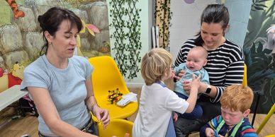 Two women and three children engaged in painting and playing in a colorful room.