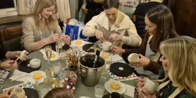 Group of women painting pottery together around a table.