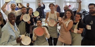 Group of people proudly displaying their decorated plates and mugs in a bright room.