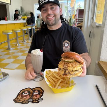 Man smiling with a large burger, fries, and milkshake.