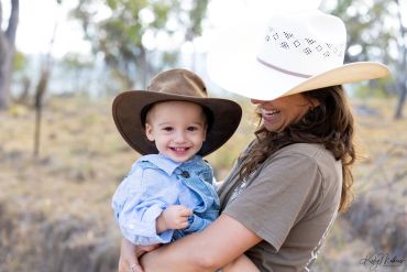 A woman holding a smiling child, both wearing hats outdoors.