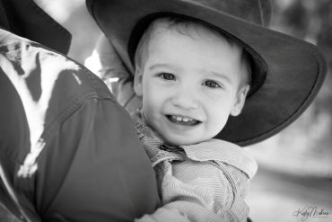 Smiling toddler wearing a cowboy hat, held by an adult.
