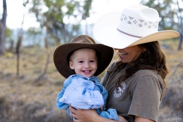 Smiling child in cowboy hat held by woman outdoors.