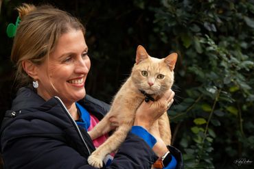 Woman smiling while holding an orange cat outdoors.