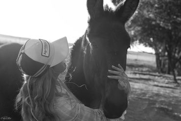 A woman gently embraces a donkey outdoors in black and white.