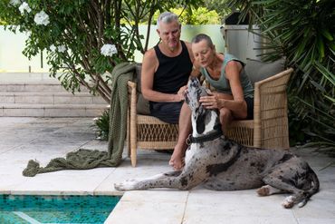 Couple sitting by the pool, affectionately interacting with their large dog.
