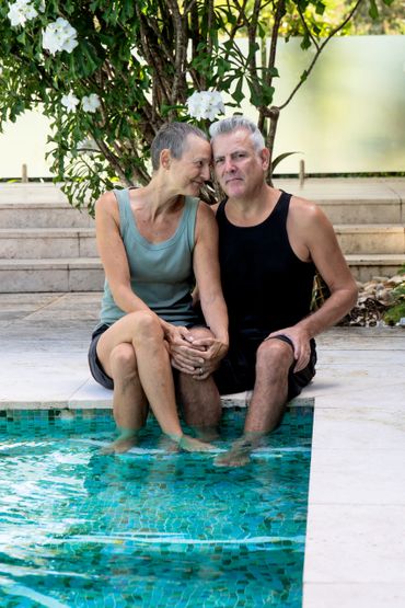 Older couple sitting by a pool, holding hands and relaxed.