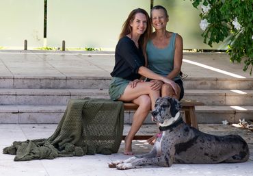 Two women sitting together outside with a large dog lying nearby.
