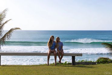 Two people sitting on a bench by the ocean on a sunny day.