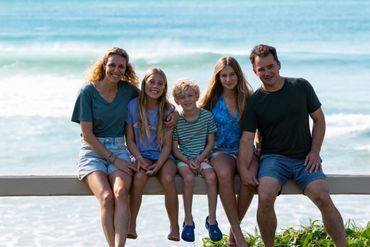 A family of five sitting on a bench by the ocean, smiling at the camera.