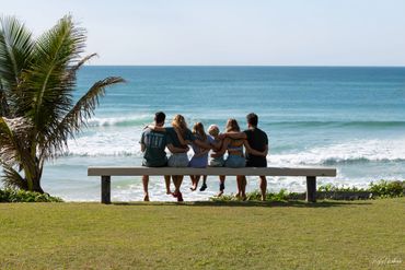 Five friends sitting on a bench, enjoying an ocean view together.