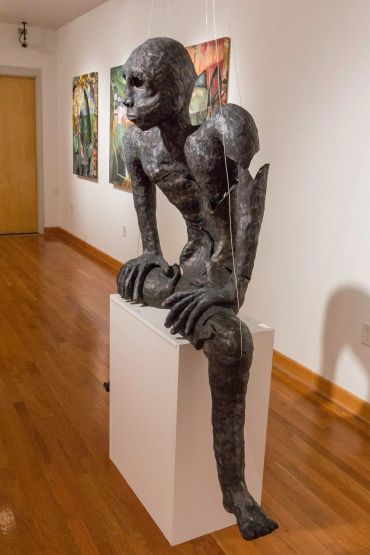 Creepy humanoid sculpture with elongated limbs in gallery.