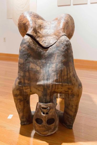 Wooden sculpture of a figure bending over with a mask on the floor.