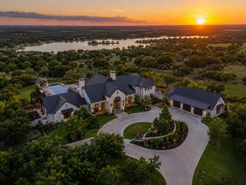 A luxury mansion at sunset with a circular driveway surrounded by greenery.
