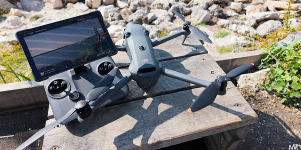Advanced drone and remote controller with screen on a wooden bench outdoors.