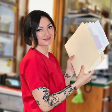 Woman in red scrubs holding file folders.