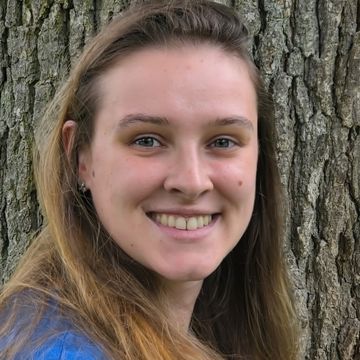 Young woman smiling outdoors with tree background.