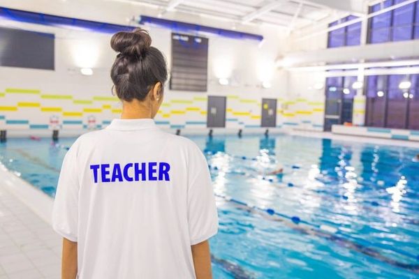 Swimming teacher overseeing a pool session indoors.