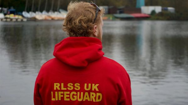 Lifeguard in a red hoodie overlooking a calm lake.