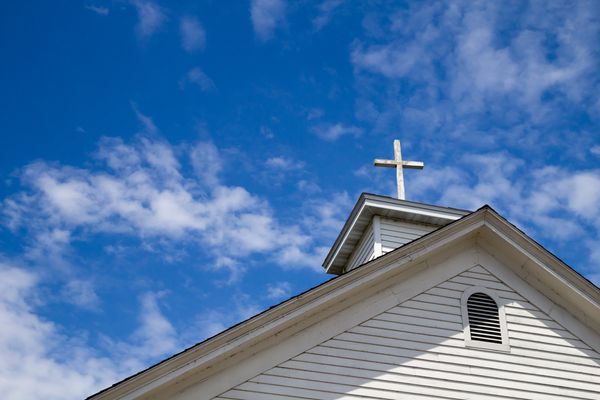 White church steeple with a cross against a blue sky with clouds.